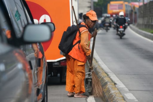 Petugas kebersihan jalan menyapu sampah-sampah di jalan.