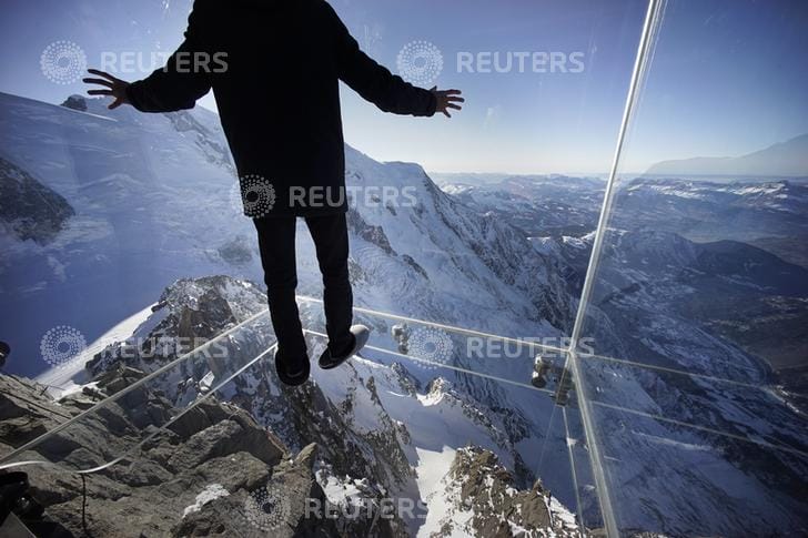 A journalist, wearing slippers to protect the glass floor, stands in the 'Step into the Void' installation during a press visit at the Aiguille du Midi mountain peak above Chamonix, in the French Alps